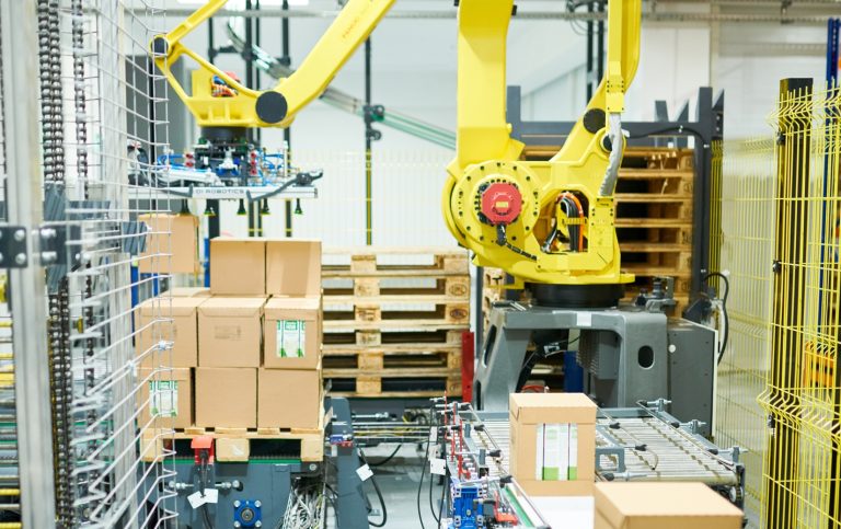 Interior of plant warehouse: industrial picking robot at work, cardboard boxes on conveyor belt, no people